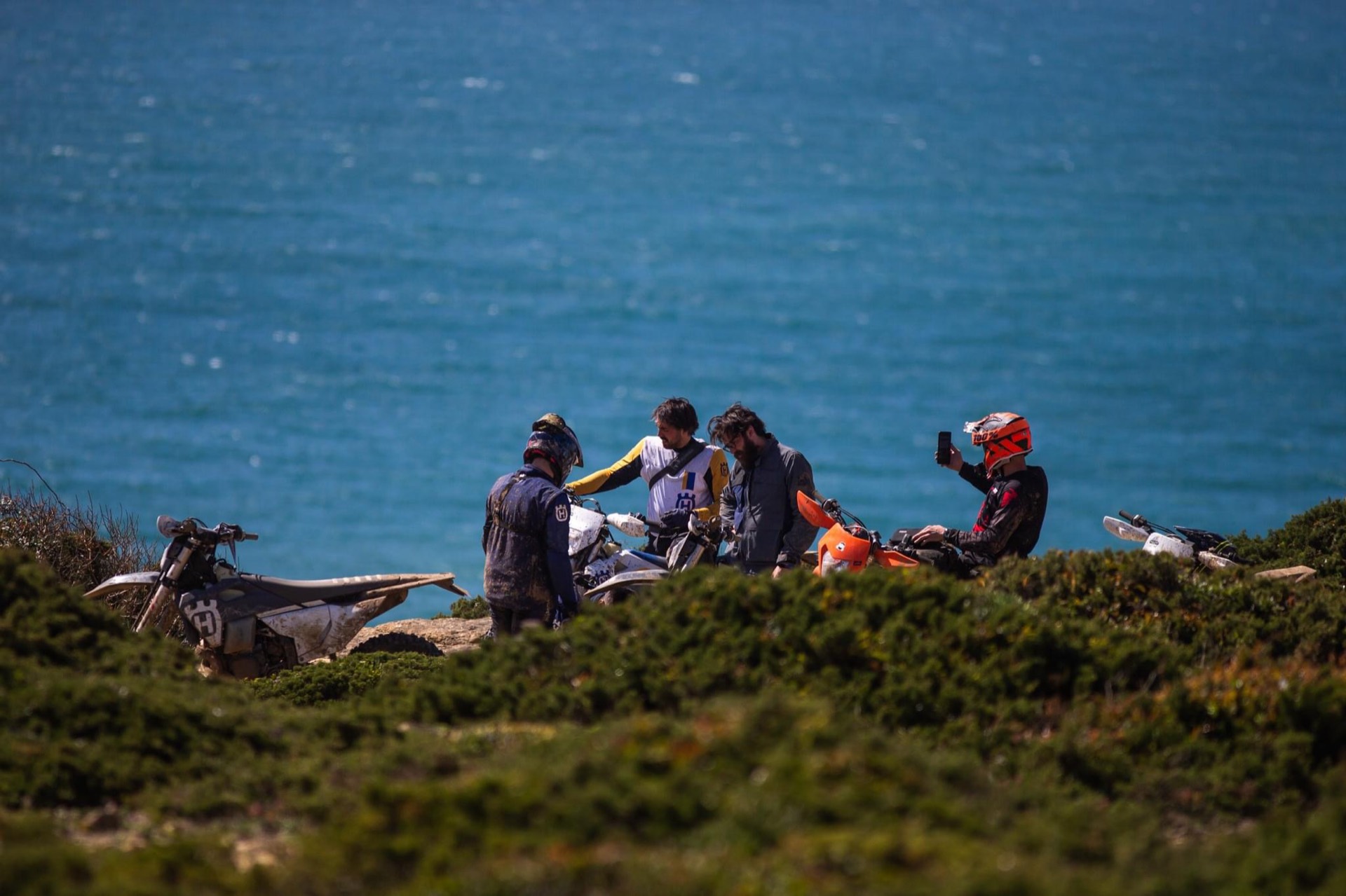 A group of riders sits on a grassy cliff above the sea.