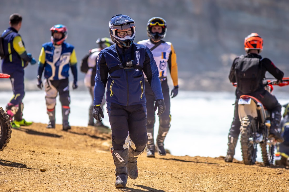 Riders in full gear stand together on a beach before heading out.