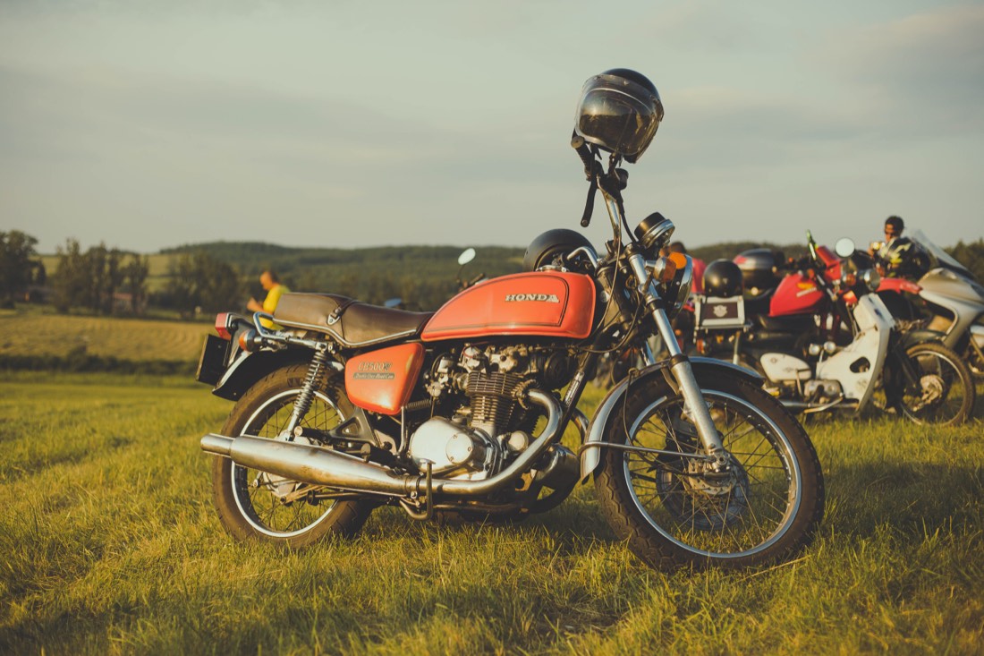 A vintage orange motorcycle parked in a field at a 100 Sparks gathering.