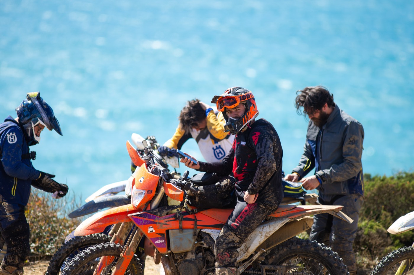 Riders talk and share a moment beside their bikes by the sea.
